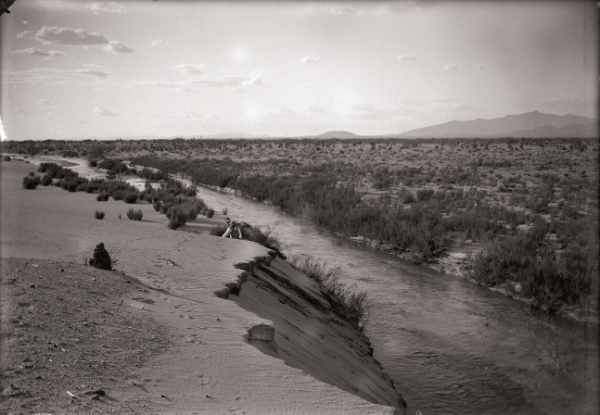 Archival sepia tone colored photograph of a river with a man emerging from the high bank.