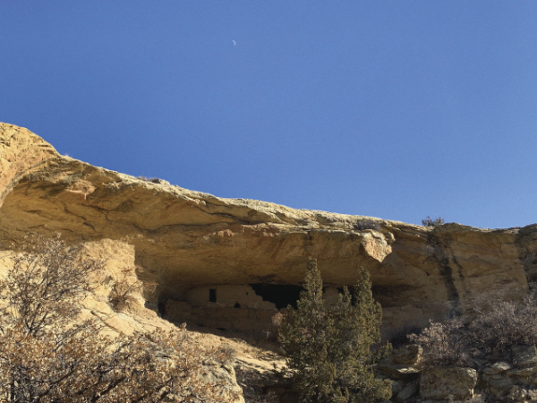 Color photograph of dwellings enveloped by rock formation under blue sky
