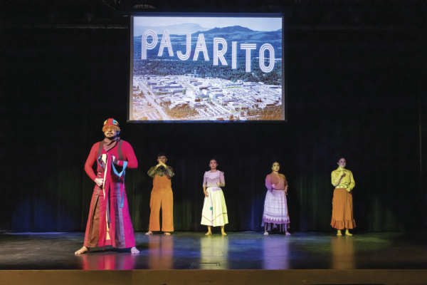 Five dancers on a stage with a projection above them of an aerial photograph with the word Pajarito in a ruled display font.