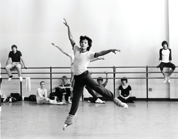 Black and white photo of a ballet class with a principal dancer and seated dancers in background