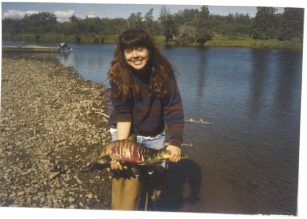 Teenage woman holding a freshly caught fish on the bank of a lake