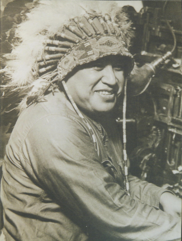 Vintage photo of a smiling man sitting at a linotype machine with a feathered headdress