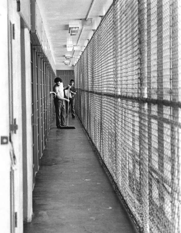 the long hallway of a cellblock with two men sweeping