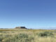 Landscape photograph with a clear blue sky, a foreground of high desert native plants and a mesa at the horizon.