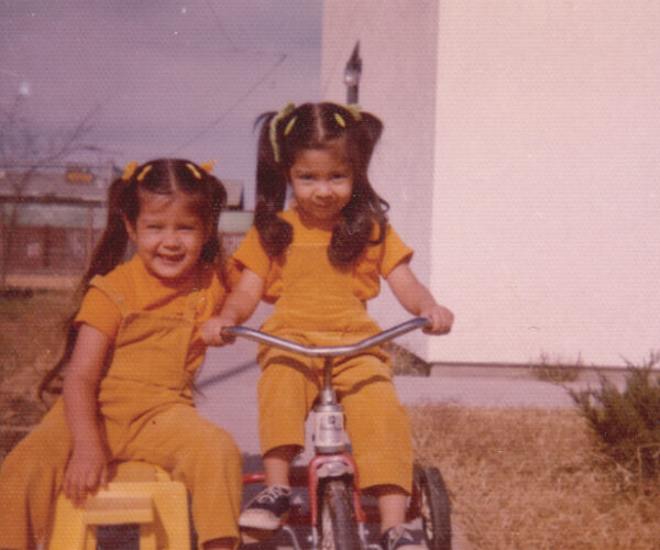 color photo of two girls on tricycles in matching yellow outfits in the mid 70s