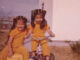 color photo of two girls on tricycles in matching yellow outfits in the mid 70s