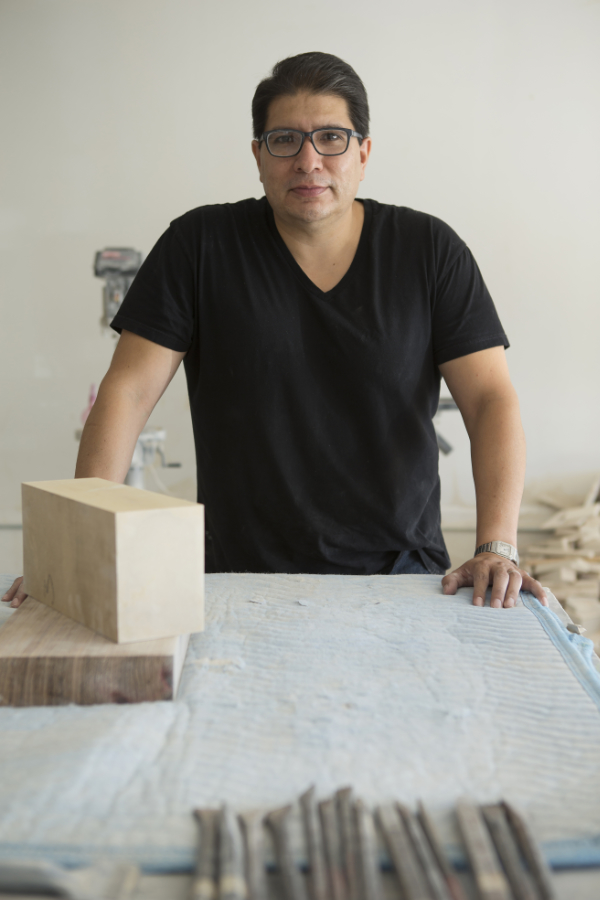 Portrait of a man in glasses and a black tshirt standing behind a work table with various forms and tools