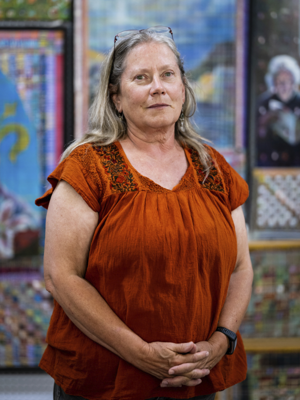 Portrait of a woman standing, hands interwoven, in front of various colorful artworks.