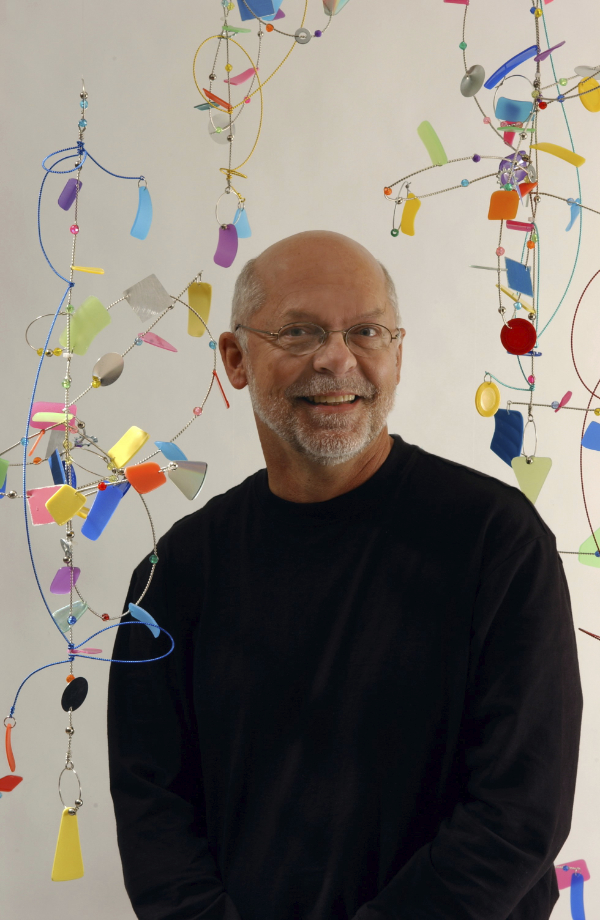 Color portrait of a man smiling amidst hanging colorful art