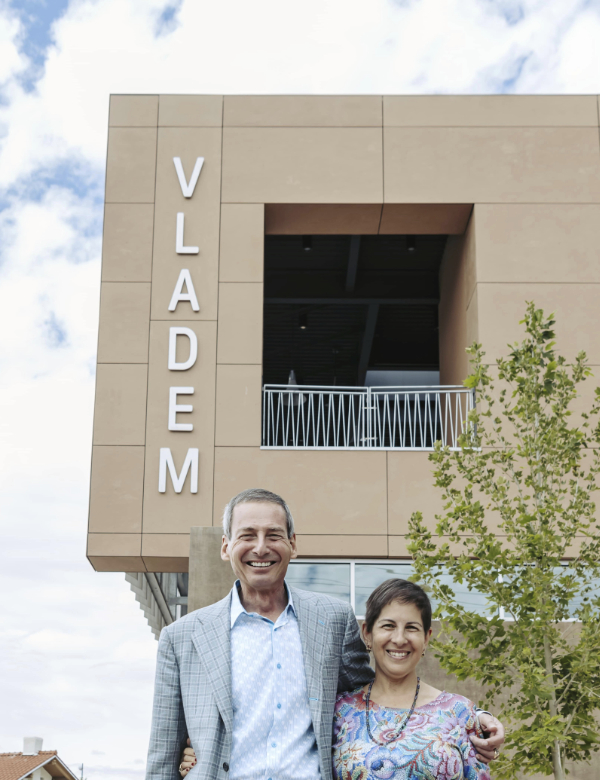 Portrait of a couple smiling in front of a building with vertical signage that says Vladem.