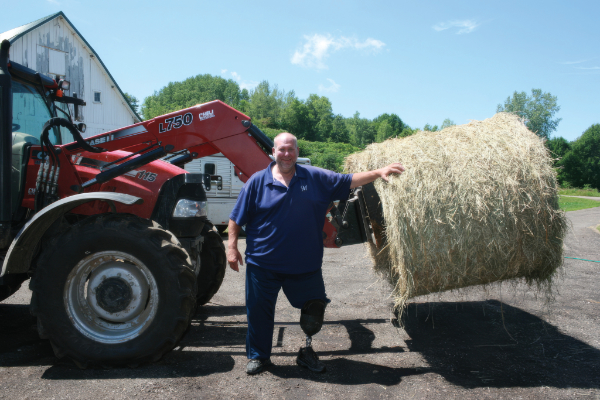 Wisconsin AgrAbility client using a bale spear to move large round hay bales.