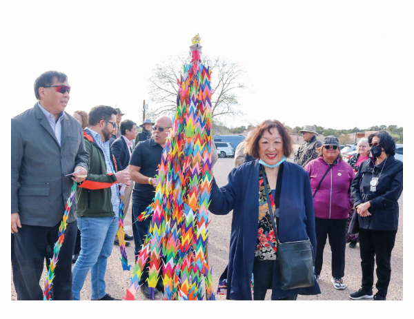 color photo of Louis posing next to pole of a thousand colorful origami cranes