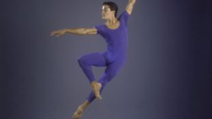 Male ballet dancer mid jump with left arm overhead and right arm extended perpendicularly