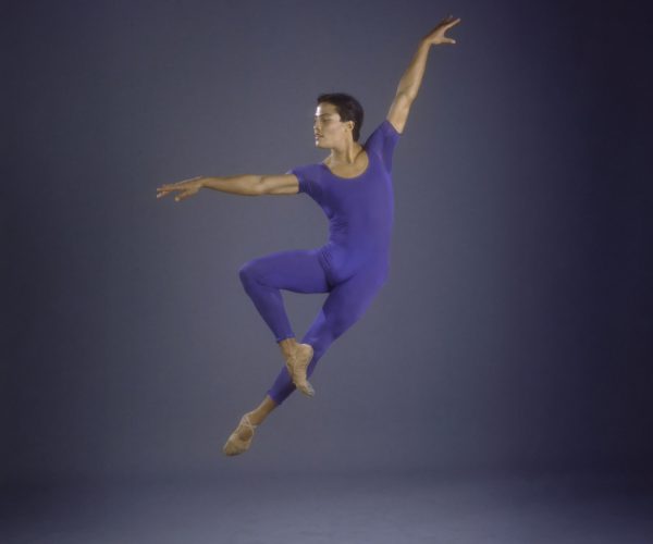 Male ballet dancer mid jump with left arm overhead and right arm extended perpendicularly