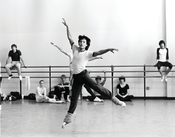 Black and white photo of a ballet class with a principal dancer and seated dancers in background