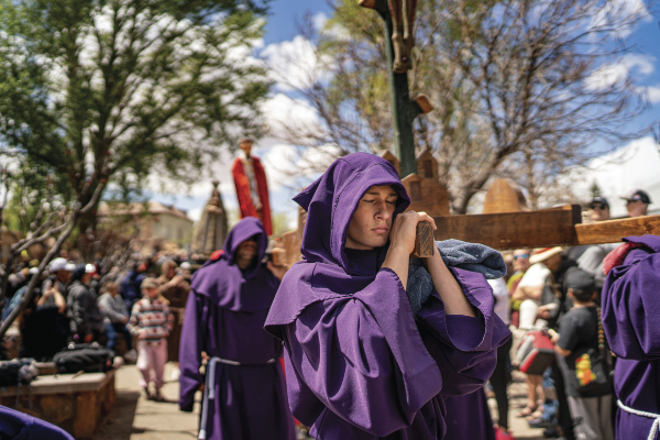 religious practitioner carrying a wodden cross with others in purple religious garb