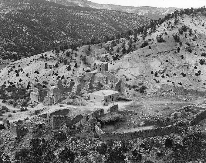 Black and white photo of ancient stone ruins situated on a hillside, surrounded by sparse trees and rocky terrain. [gen-ai]