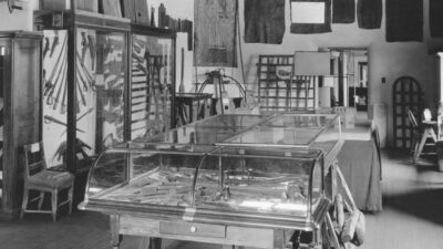 Black and white photo of a historical museum room with glass display cases, wooden furniture, and artifacts mounted on the walls. [gen-ai]