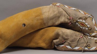 A pair of large leather mittens with beaded trim and decorative designs, featuring tan and yellow coloring and a circular hole on one mitten. [gen-ai]
