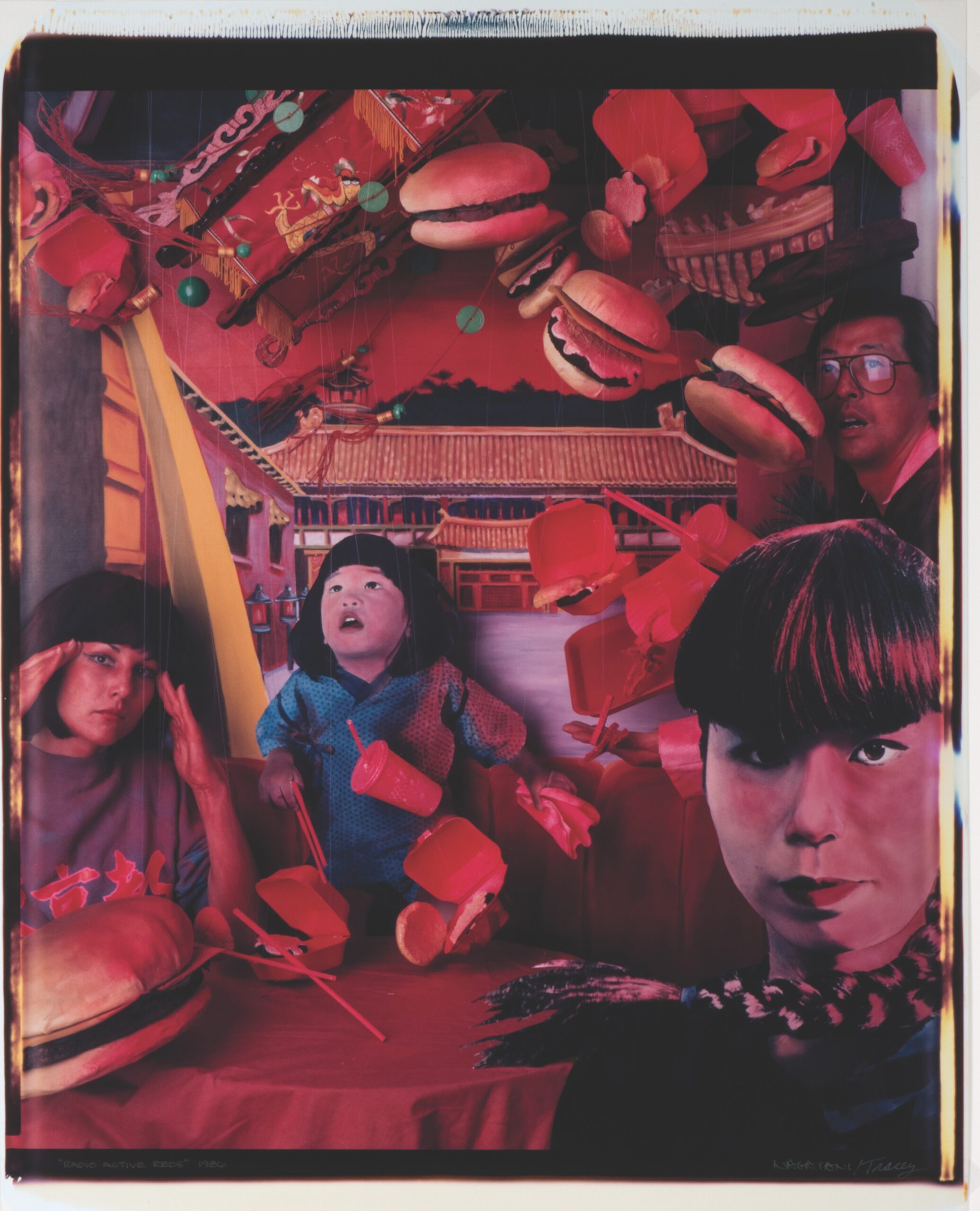 Surreal scene of people sitting at a table as fast food items float around them in a vivid, red-toned environment with a building in the background. [gen-ai]