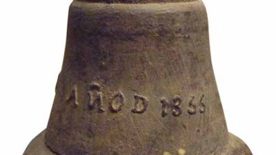 A weathered metal bell with a rounded top and an inscription reading AÑO D 1835 on its side. [gen-ai]