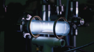 A glowing plasma is contained within a glass tube, surrounded by metal rings and scientific equipment in a dark laboratory setting. [gen-ai]