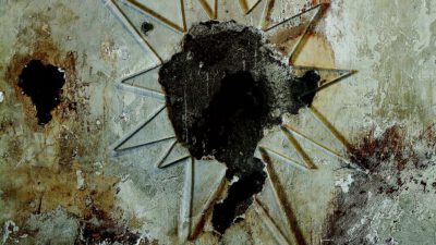 A bullet hole with shattered glass is set in a weathered wall. A sign above reads: Legend has it that this hole was put here by a bullet from Billy the Kid’s six-shooter when he escaped. [gen-ai]