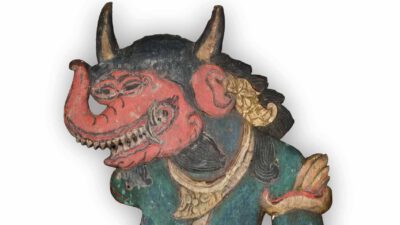 A painted wooden figure of a mythical creature with a red face, long horn, sharp teeth, and elaborate jewelry, from traditional Indonesian art. [gen-ai]
