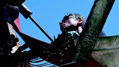 A person wearing sunglasses works on a large outdoor sculpture with metal and painted elements against a clear blue sky. [gen-ai]