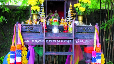 A small outdoor shrine decorated with yellow flowers, garlands, colorful cloth, figurines, candles, and two pumpkins, set against a bamboo background. [gen-ai]