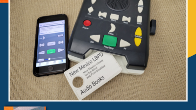A digital audio player, a smartphone displaying playback controls, and a New Mexico Library for the Blind and Print Disabled audio book cartridge are arranged on a beige surface. [gen-ai]