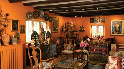 A colorful living room with orange walls, wooden ceiling beams, eclectic furniture, patterned rugs, decorative plates, paintings, and various ornaments. [gen-ai]