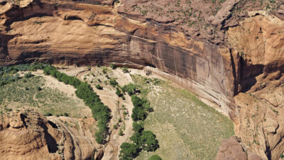 Aerial view of a large red rock canyon with steep cliffs, green trees, and a sandy floor, showing clear layers of sediment and sparse vegetation. [gen-ai]