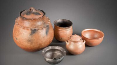 A set of five clay pots and bowls of varying shapes and sizes displayed against a neutral gray background. [gen-ai]