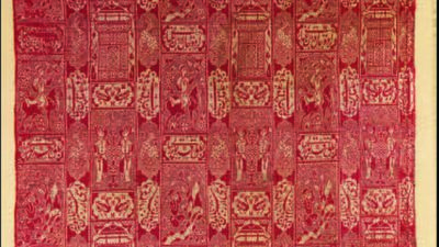 A rectangular textile featuring a repeating geometric and floral pattern in red and gold tones, arranged in vertical columns and horizontal rows. [gen-ai]