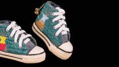 A pair of childrens high-top sneakers with green fabric, white laces, multicolored animal designs, and decorative beads, displayed on a black background. [gen-ai]