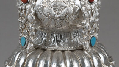 Detailed close-up of an ornate silver object featuring intricate floral engravings and inlays of turquoise and red stones. [gen-ai]