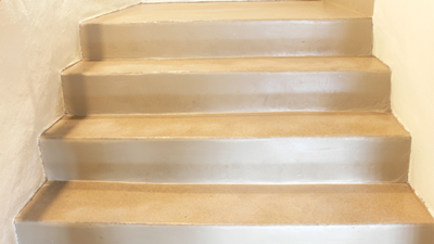 Four beige-painted concrete stairs leading up to a small landing, with white walls on both sides. [gen-ai]