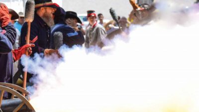 Men in historical military uniforms fire a cannon, producing a large cloud of smoke, while onlookers watch in the background. [gen-ai]