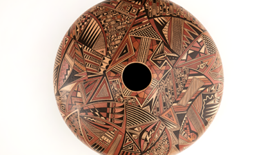 Round ceramic vessel with a central opening, featuring intricate geometric patterns in red, black, and tan tones, photographed on a white background. [gen-ai]