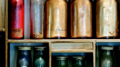 A wooden shelf holding glass jars and bottles filled with colored powders or pigments, some labeled with numbers and colors. [gen-ai]