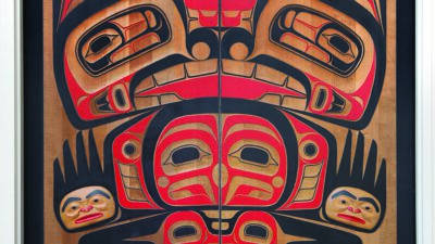 Large wooden doors feature a traditional Indigenous Pacific Northwest Coast design in red, black, and tan, depicting stylized animal and human figures in symmetrical patterns. [gen-ai]