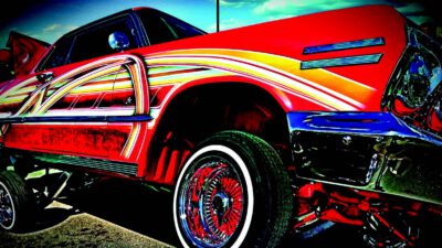 A brightly painted lowrider car with custom red, yellow, and white designs, lifted on hydraulics, with chrome wheels and trim. [gen-ai]