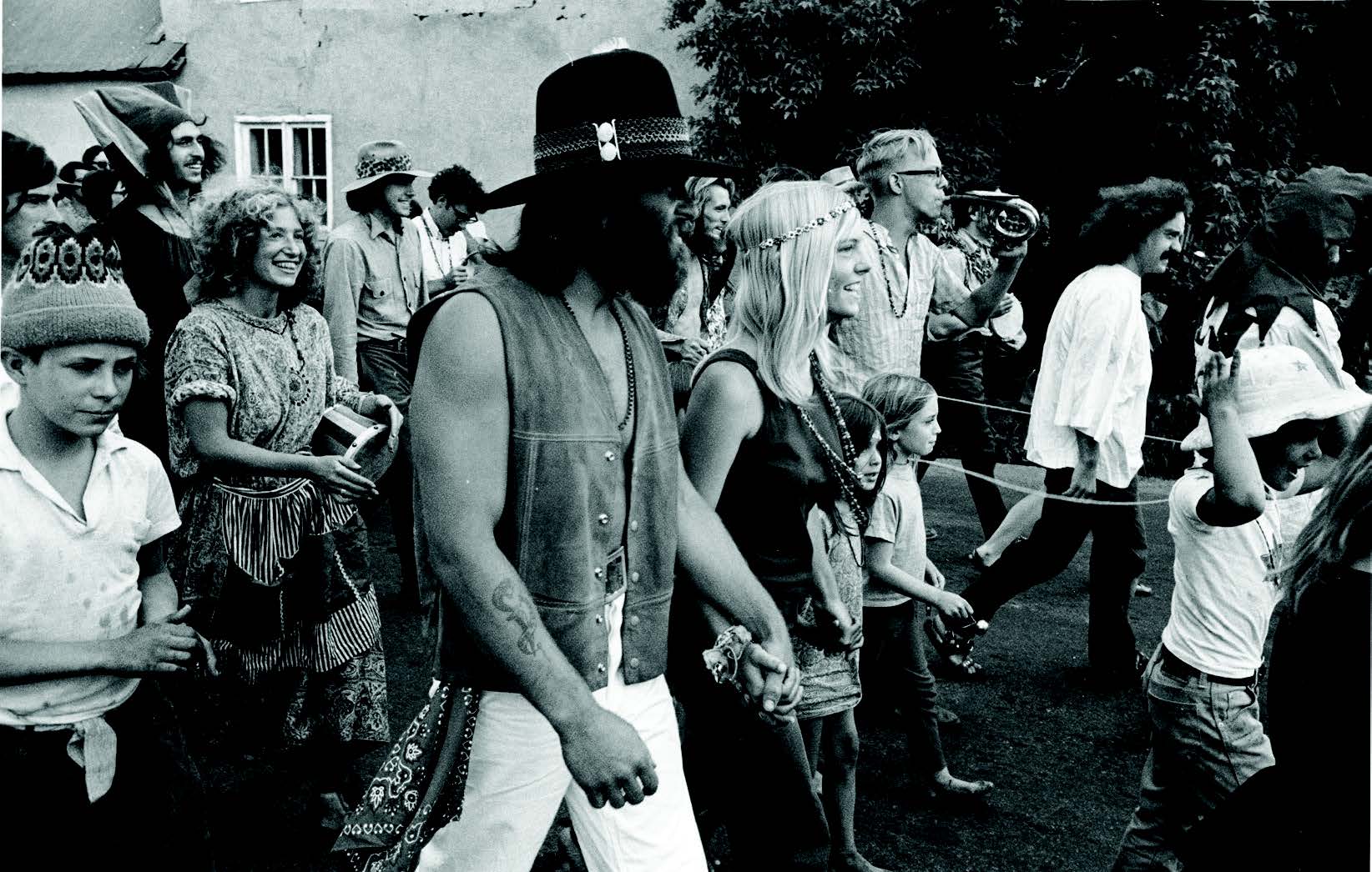 A group of people in bohemian attire walk together outdoors, some holding hands and smiling, in a black-and-white photo. [gen-ai]