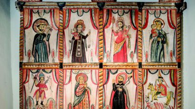 A painted wooden altarpiece featuring nine religious figures in separate panels, each with distinct clothing and poses, set against a colorful, patterned background. [gen-ai]