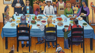 A group of people, including a man in a white cowboy hat, share a meal at a long table; others stand behind them, with mountains, houses, a dog, and a parrot in the background. [gen-ai]