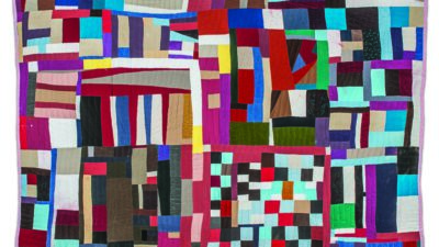 A colorful patchwork quilt featuring irregular geometric shapes and varied fabric pieces in a range of bright and muted colors. [gen-ai]