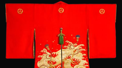 A traditional red Japanese kimono with gold embroidered waves and crests, displayed against a black background. [gen-ai]