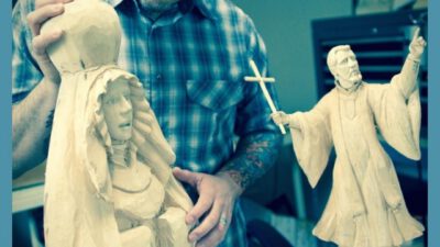 A man in glasses and a plaid shirt inspects two wooden religious sculptures, one of Mary and another of Jesus holding a cross. Text reads Encounter Culture Season 1 Episode 2. [gen-ai]