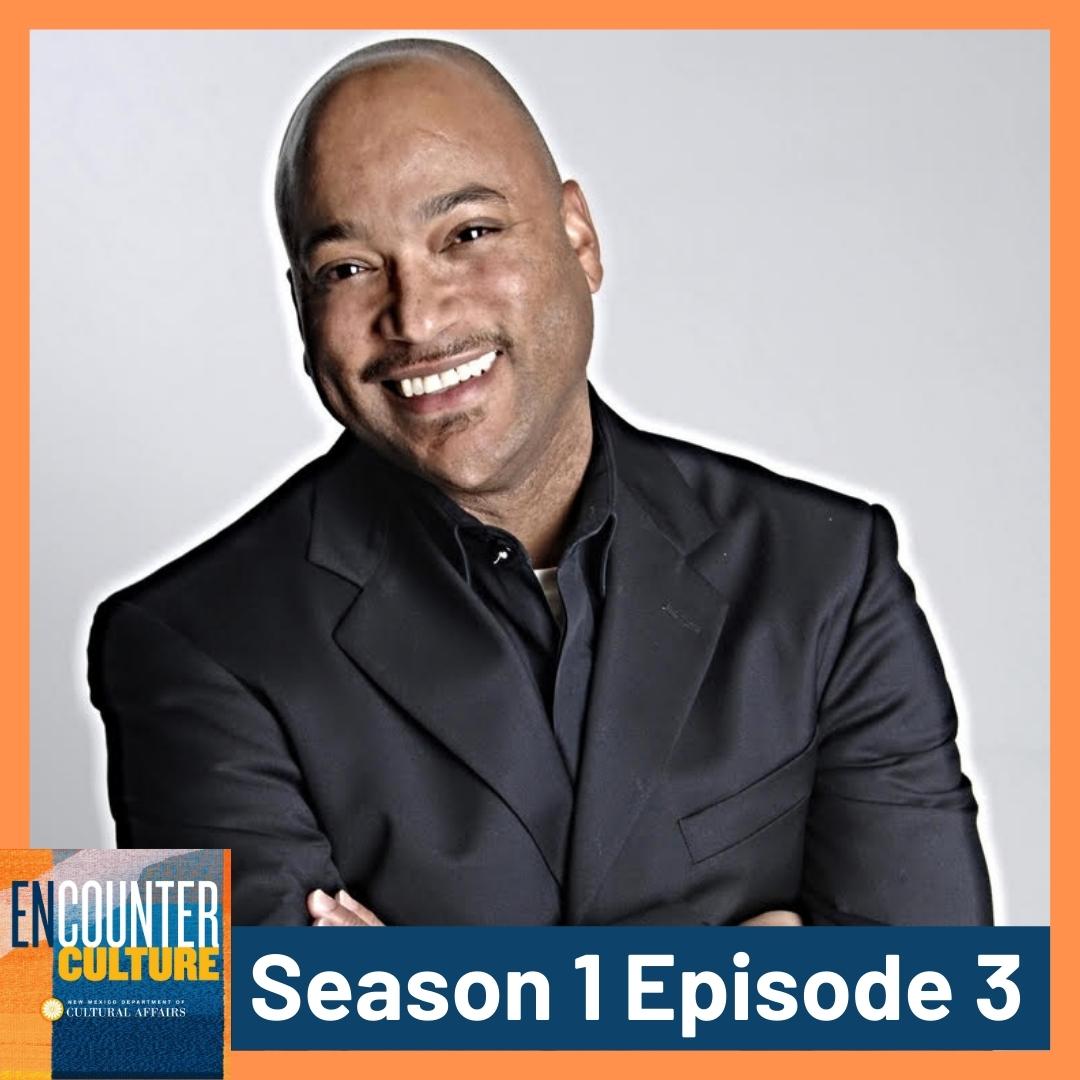A smiling man in a black suit poses with arms folded. Text reads “ENCOUNTER CULTURE Season 1 Episode 3” in a blue and orange border. [gen-ai]